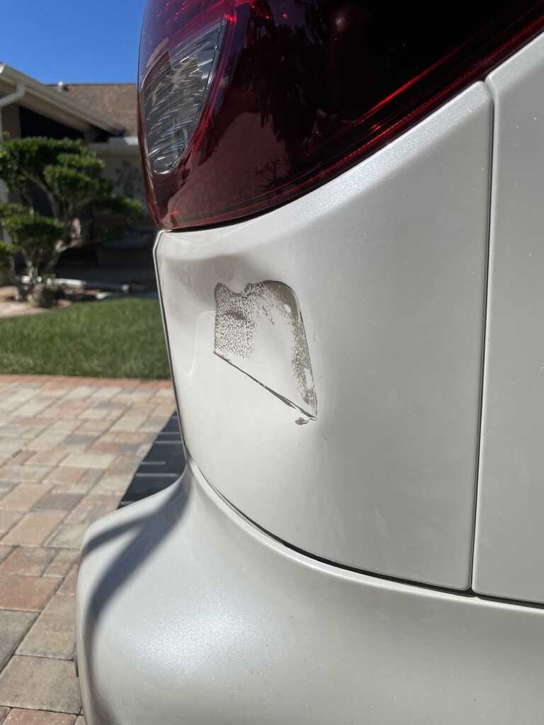 Rear quarter panel of a white Toyota Sequoia with a clear dent and scuffed paint, photographed in a residential driveway